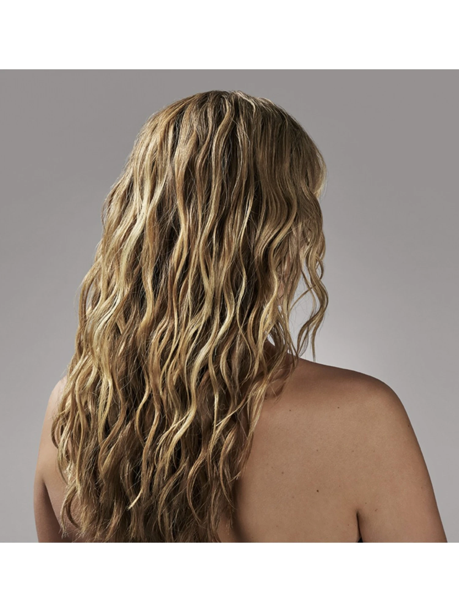 Espalda de mujer con cabello rubio mostrando ondas surferas naturales creadas con Oribe Après Beach.