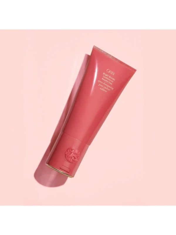 Vista en ángulo del envase de Oribe Bright Blonde Conditioner for Beautiful Color de 200 ml sobre un fondo rosado con sombras estéticas