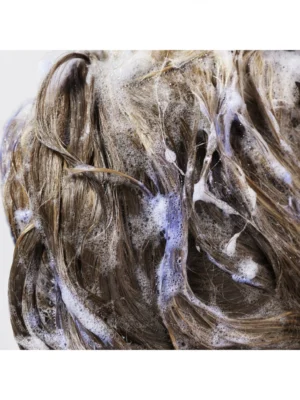 Detalle de la aplicación de Oribe Bright Blonde Shampoo for Beautiful Color en el cabello, mostrando su acción neutralizadora y espuma violeta