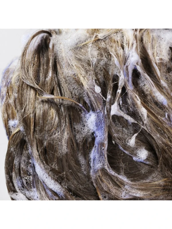 Detalle de la aplicación de Oribe Bright Blonde Shampoo for Beautiful Color en el cabello, mostrando su acción neutralizadora y espuma violeta