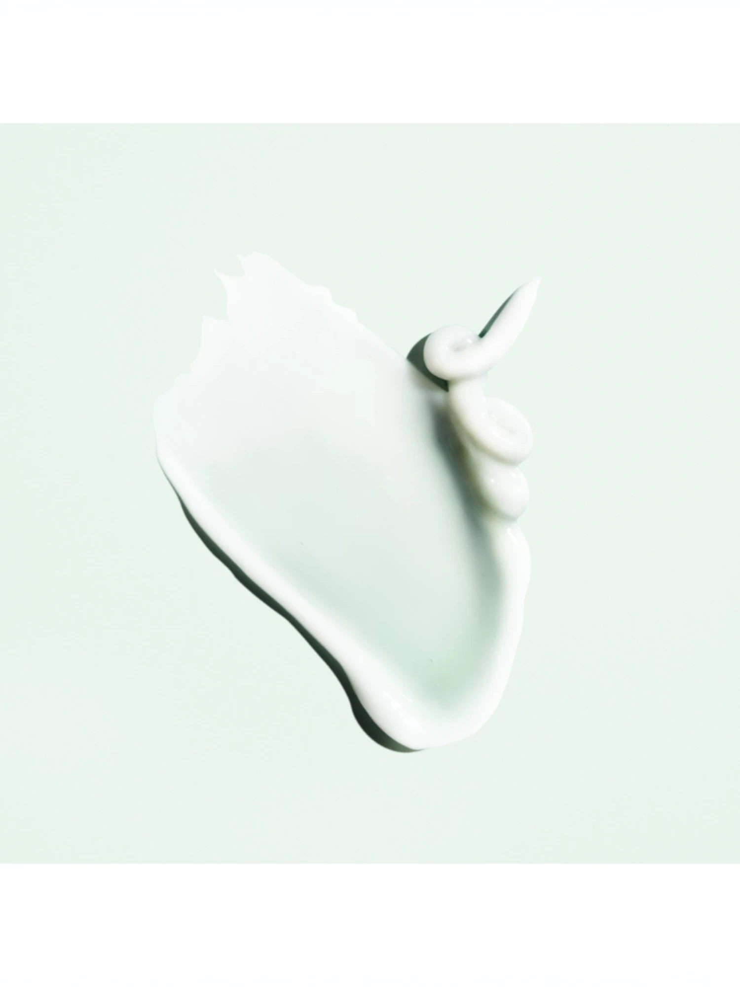 Muestra de la textura en crema blanca y sedosa de Oribe Curl Control Silkening Creme sobre fondo verde menta