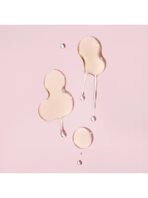 Detalle de las gotas de textura fluida y transparente del sérum protector del color de Oribe sobre fondo rosado