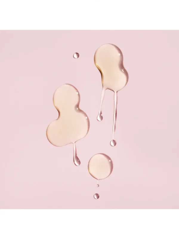 Detalle de las gotas de textura fluida y transparente del sérum protector del color de Oribe sobre fondo rosado