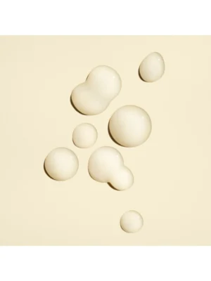 Detalle de las gotas de textura concentrada y el envase de Oribe Power Drops Damage Repair Booster sobre un fondo crema