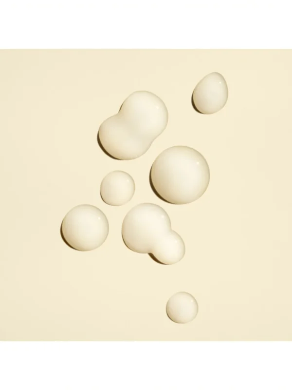 Detalle de las gotas de textura concentrada y el envase de Oribe Power Drops Damage Repair Booster sobre un fondo crema