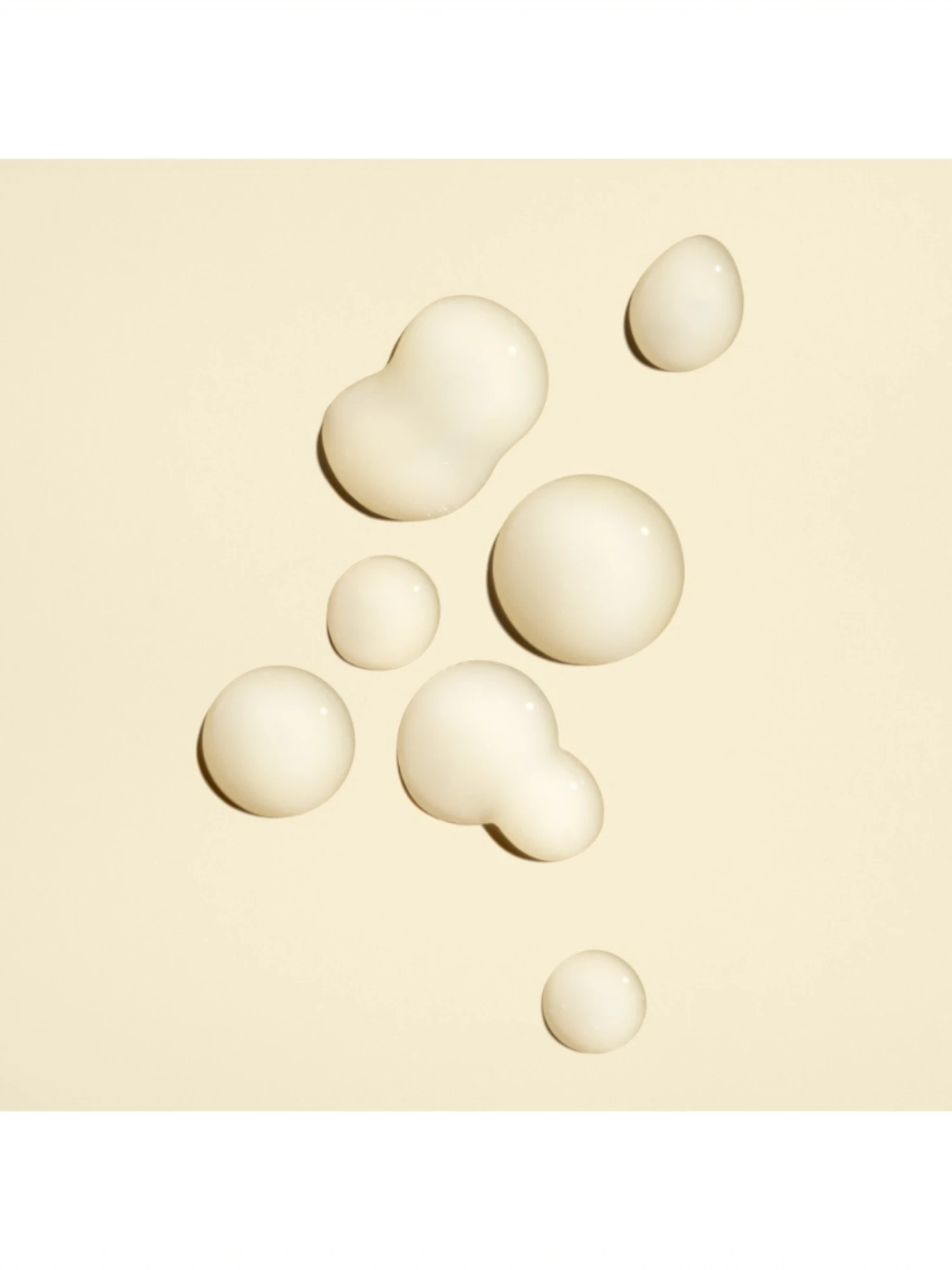 Detalle de las gotas de textura concentrada y el envase de Oribe Power Drops Damage Repair Booster sobre un fondo crema