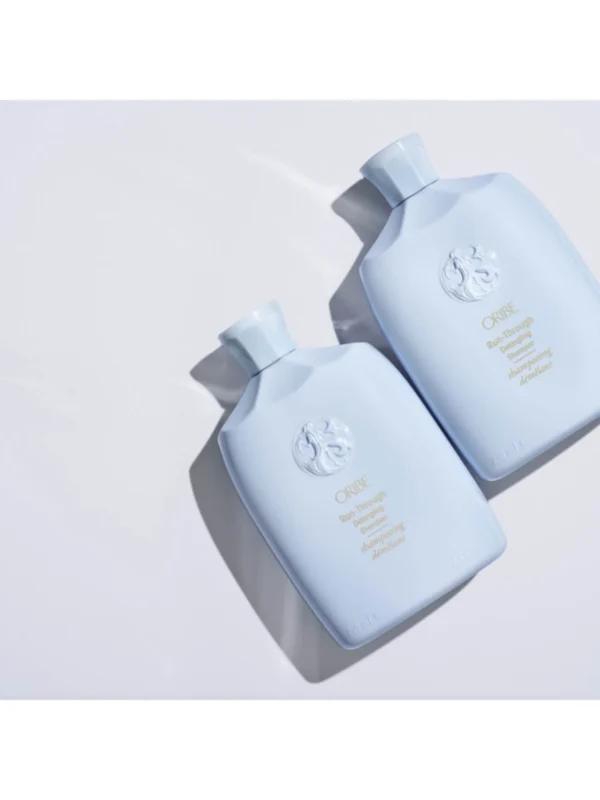 Dos botellas frontal de Oribe Run-Through Detangling Shampoo con su envase azul marino y detalles en dorado