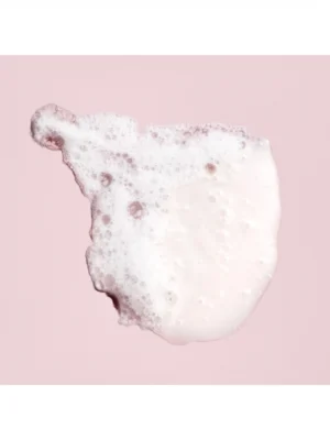 Primer plano de la espuma delicada y rica del champú protector del color de Oribe sobre fondo rosado
