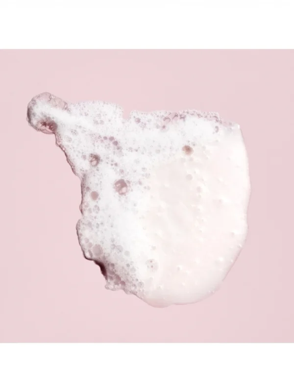 Primer plano de la espuma delicada y rica del champú protector del color de Oribe sobre fondo rosado
