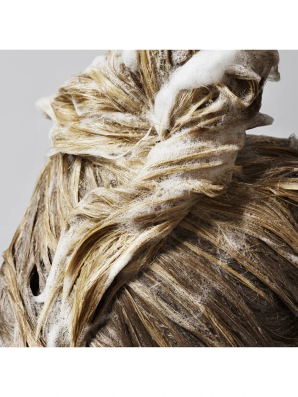 Aplicación profesional del champú Oribe para volumen, mostrando la formación de espuma densa y purificante en el cabello