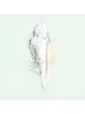 Detalle de la textura en gel y la espuma blanca de Oribe Shampoo For Moisture And Control sobre fondo verde claro