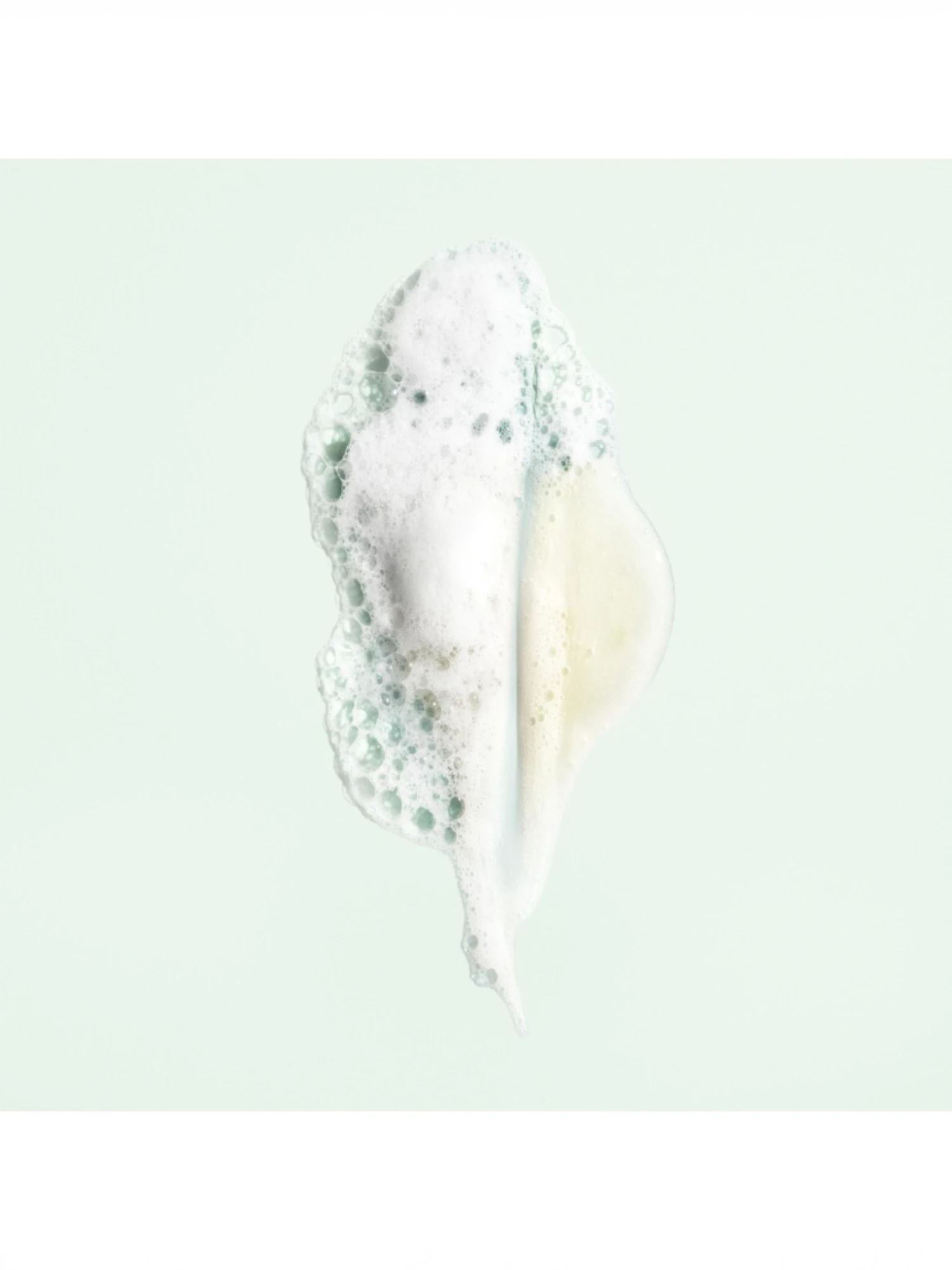 Detalle de la textura en gel y la espuma blanca de Oribe Shampoo For Moisture And Control sobre fondo verde claro