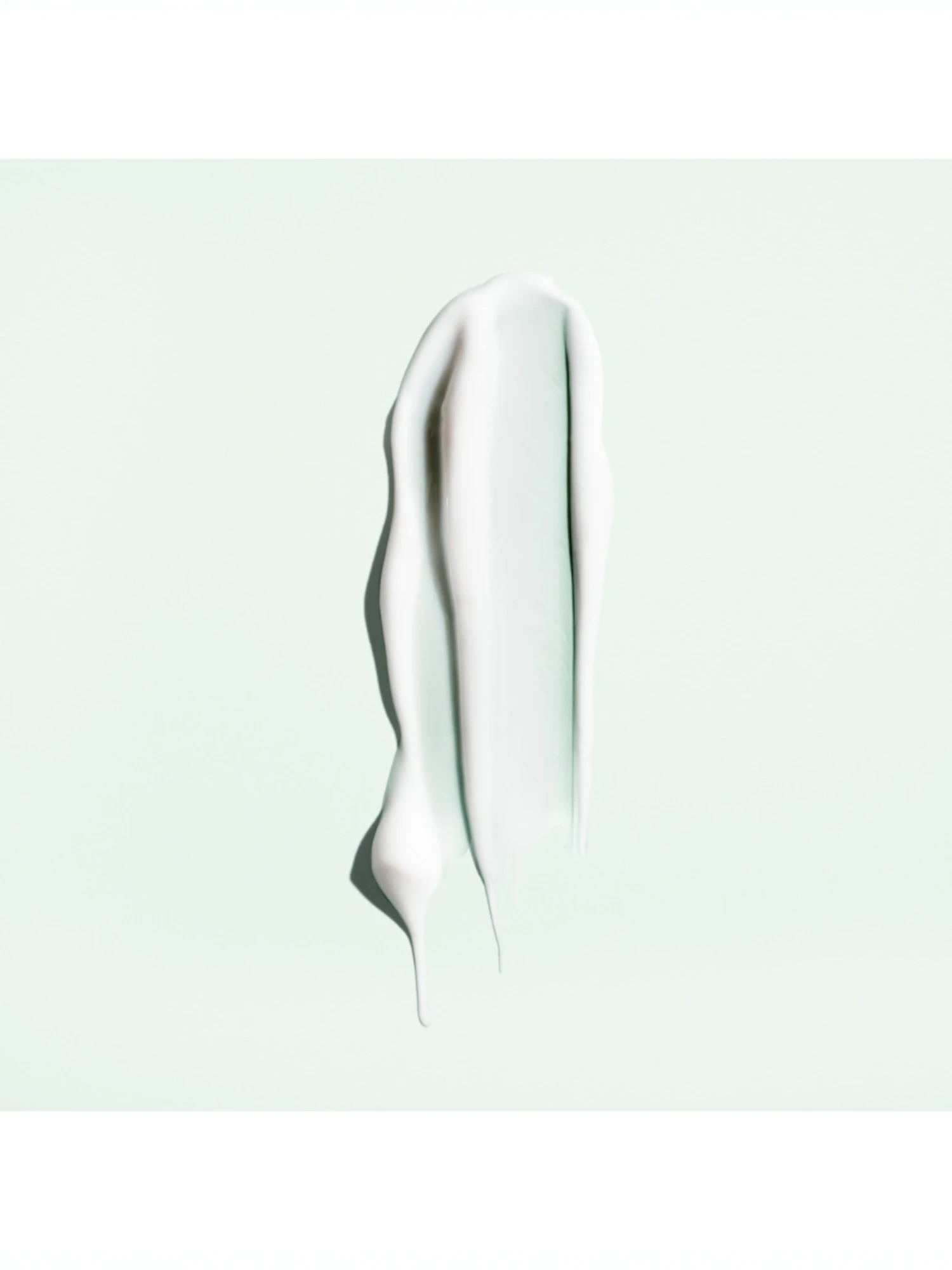 Detalle de la textura en crema fluida blanca de Straight Away Smoothing Blowout Cream sobre fondo verde claro