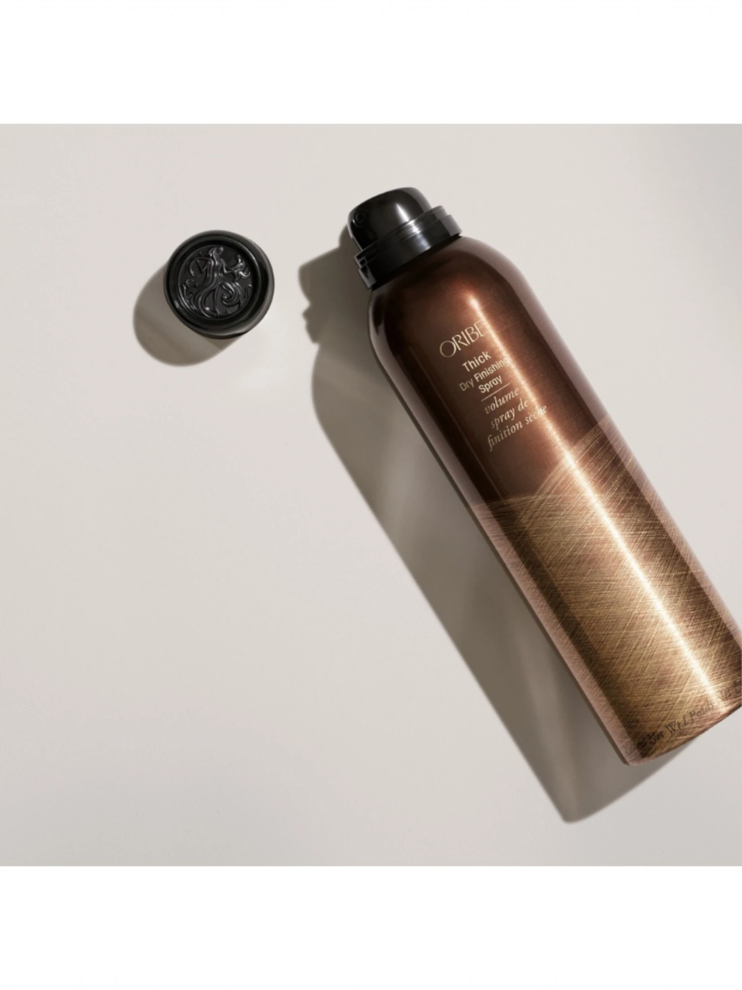 Vista en ángulo del spray Oribe Thick Dry Finishing Spray con su tapón decorado, serie Magnificent Volume