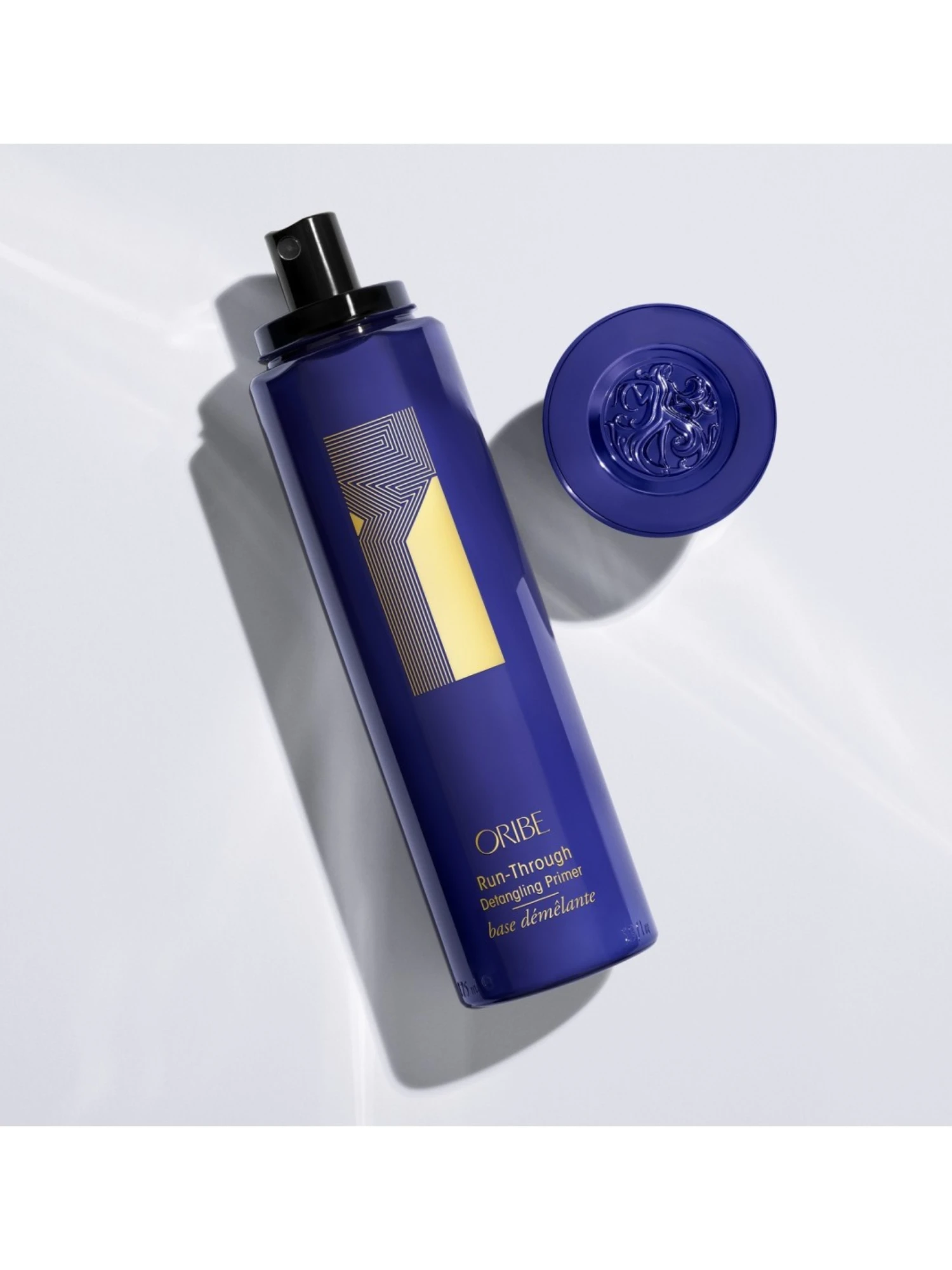 Vista cenital del spray Run-Through Detangling Primer de Oribe junto a su tapa con emblema.