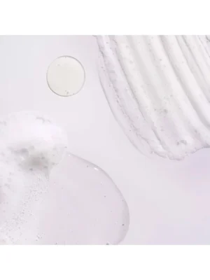 Detalle macro de la textura viscosa transparente y muestras de espuma blanca del champú sobre fondo liso.