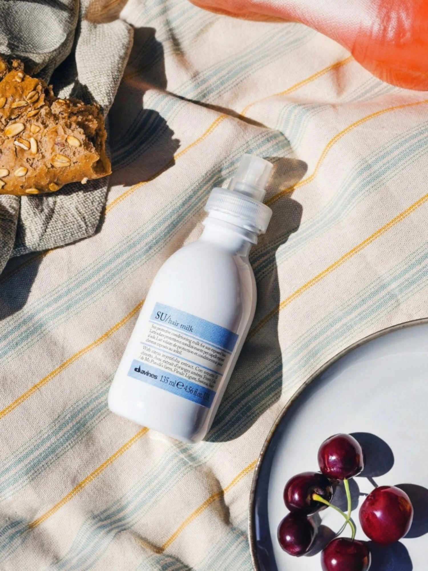 Bodegón veraniego de Davines SU Milk sobre mantel con cerezas, ideal para la protección capilar en exteriores