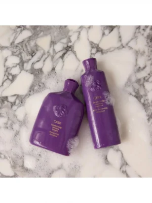 Acondicionador Oribe Serene Scalp Densifying Conditioner con espuma sobre superficie de mármol